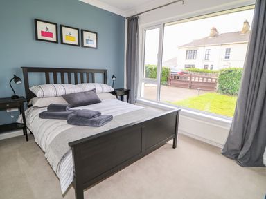 A bedroom with a double bed two bedside tables lamps and a large window at Seacoast Cottage in Castlerock