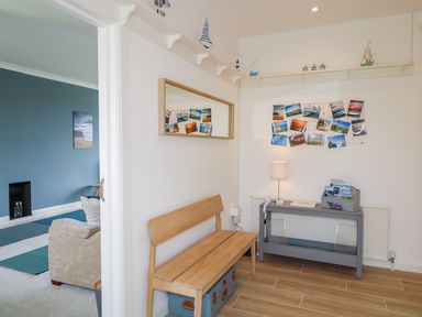An entryway with a wooden bench and gray console table with lamp and photos at Seacoast Cottage in Castlerock