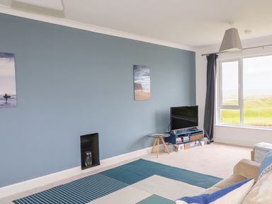 A living room with blue painted wall a television on a stand and a window with curtains at Seacoast Cottage in Castlerock