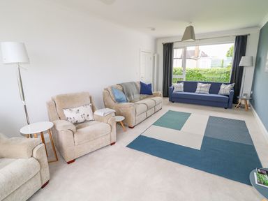 A living room with beige armchairs blue sofa and blue patterned rug at Seacoast Cottage in Castlerock