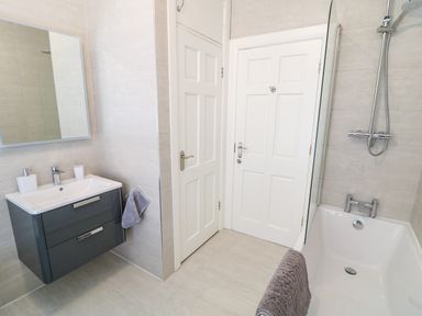 A bathroom with a sink cabinet mirror two white doors bathtub shower and towel at Seacoast Cottage in Castlerock