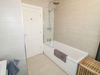 A bathroom with a bathtub shower combination a towel hanging on the side and a wooden laundry basket at Seacoast Cottage in Castlerock