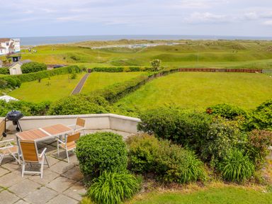 A patio with outdoor furniture and a barbecue overlooking grassy fields and the ocean at Seacoast Cottage in Castlerock