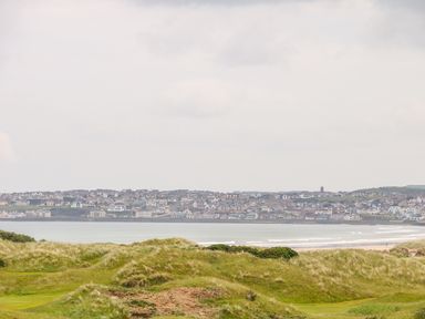 A coastal town across water with grassy dunes in the foreground at Seacoast Cottage in Castlerock