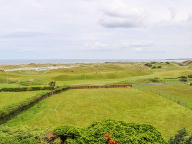 A landscape with a green field, rolling hills, and a view of the sea at Seacoast Cottage in Castlerock