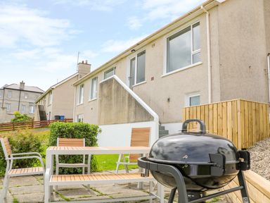 An outdoor patio area with a barbecue grill a table with chairs and benches near a row of houses