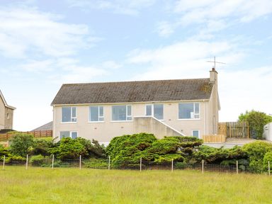A house with multiple windows and a sloped roof surrounded by shrubs and grass at Seacoast Cottage in Castlerock