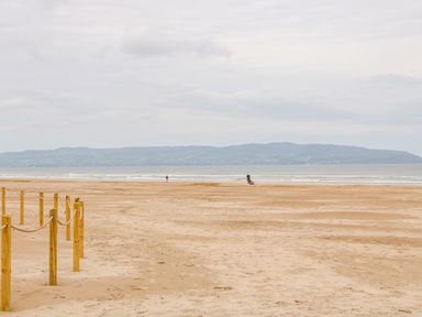 A sandy beach with wooden posts and rope near the shore and a distant view of hills across the water at Seacoast Cottage in Castlerock