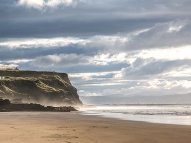 A sandy beach with cliffs and cloudy sky at Seacoast Cottage in Castlerock