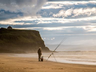 A person fishing on a beach with fishing rods and a rocky cliff in the background at Seacoast Cottage in Castlerock