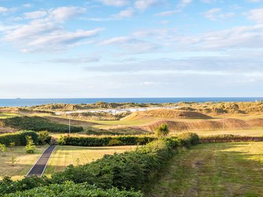 A garden with bushes and a pathway leading to sand dunes and the sea at Seacoast Cottage in Castlerock