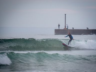 A person surfing on a wave near a pier with two people fishing at Seacoast Cottage in Castlerock