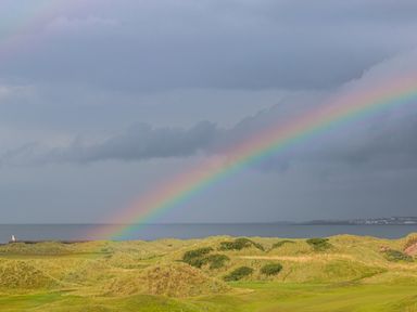 A rainbow over grassy hills by the sea with a cloudy sky at Seacoast Cottage in Castlerock