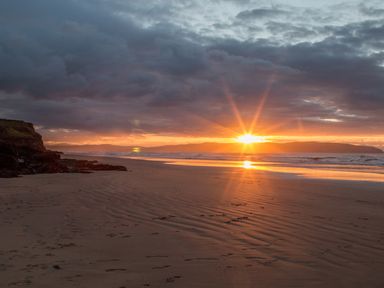 A beach with sand and rocks at sunset with the sun near the horizon at Seacoast Cottage in Castlerock