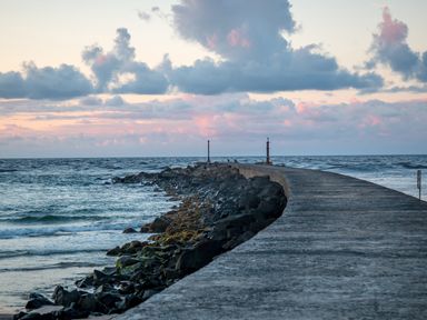 A concrete pier extending into the ocean with rocks along the side under a cloudy sky at Seacoast Cottage in Castlerock