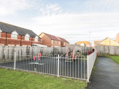 A small fenced playground with a spring rider and slide near houses at 39 Longbeach Drive in Beadnell