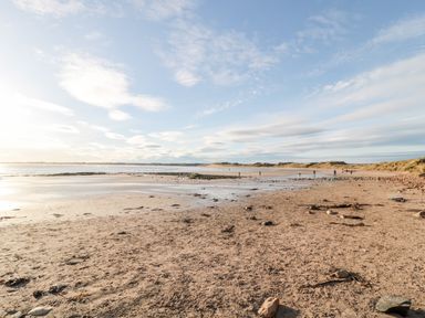 A sandy beach with scattered rocks and people walking near the shoreline at 39 Longbeach Drive in Beadnell