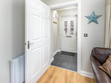 A hallway with a white door leading outside a brown leather sofa and blue star wall decoration at 39 Longbeach Drive in Beadnell