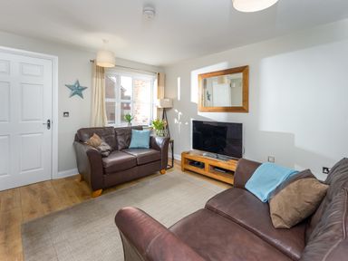 A living room with two brown leather sofas a television on a wooden stand and a wall mirror at 39 Longbeach Drive in Beadnell