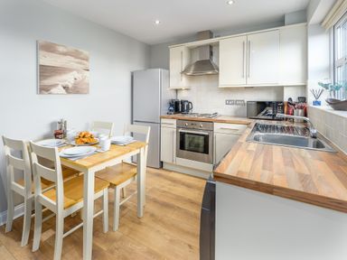 A kitchen with wooden countertops a dining table with plates cups and croissants and white cabinets at 39 Longbeach Drive Beadnell