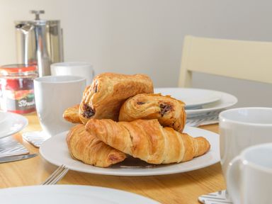 A plate of croissants and pain au chocolat on a dining table with cups and plates at 39 Longbeach Drive in Beadnell
