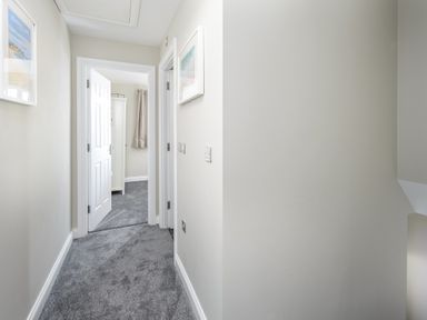 A hallway with grey carpet with two open doors showing a room with a wardrobe and a curtain at 39 Longbeach Drive in Beadnell