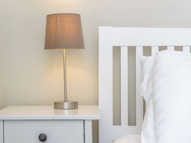 A bedside table with a lamp next to a white bed frame and pillow at 39 Longbeach Drive Beadnell