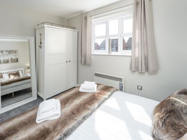 A bedroom with a bed covered with a brown fur blanket two folded white towels a white wardrobe a large mirror and a window with beige curtains at 39 Longbeach Drive in Beadnell