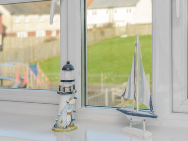 A window sill with a lighthouse ornament and a sailboat ornament at 39 Longbeach Drive in Beadnell