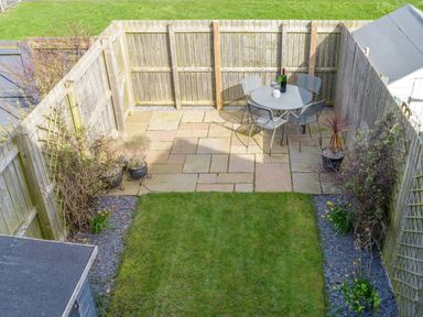 A small fenced backyard with a grass lawn a paved patio with a round table and four chairs and potted plants at 39 Longbeach Drive in Beadnell