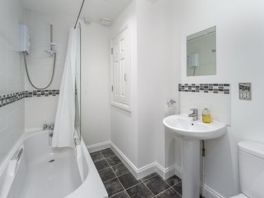 A bathroom with a bathtub shower combo sink with soap dispenser mirror and tiled floor at 39 Longbeach Drive in Beadnell