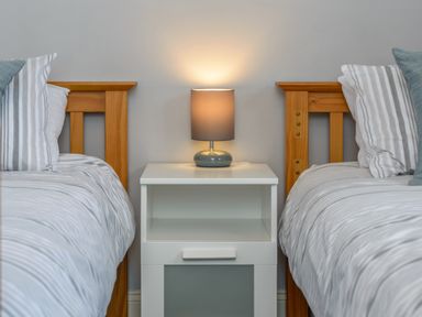 A bedroom with two single beds with striped bedding and a white bedside table with a lamp at 39 Longbeach Drive in Beadnell