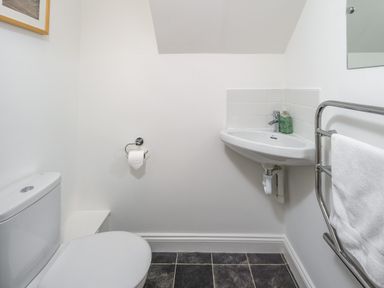 A small bathroom with a toilet a wall-mounted sink soap dispenser a towel on a rack and a tiled floor at 39 Longbeach Drive Beadnell