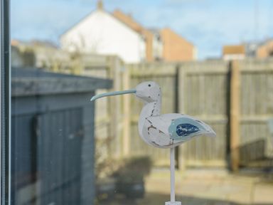 A wooden bird sculpture outside a window with a garden fence and buildings in the background at 39 Longbeach Drive in Beadnell