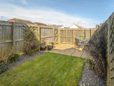 A fenced backyard with a grass lawn a paved patio area with a table and chairs and plants along the fence at 39 Longbeach Drive in Beadnell