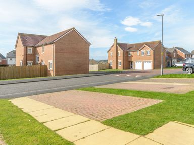 A residential street with brick houses and paved driveways with grass patches at 39 Longbeach Drive in Beadnell