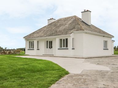 A detached white house with a sloped roof two chimneys a concrete driveway and green lawn at Dirreen House in Athea near Listowel County Kerry