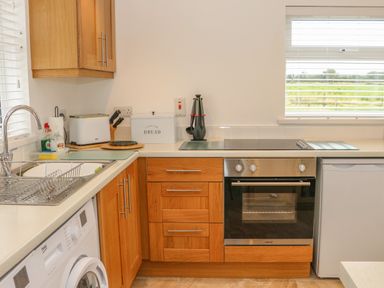 A kitchen with wooden cabinets a sink a washing machine an oven a stove a bread box and a window at Dirreen House Athea near Listowel County Kerry