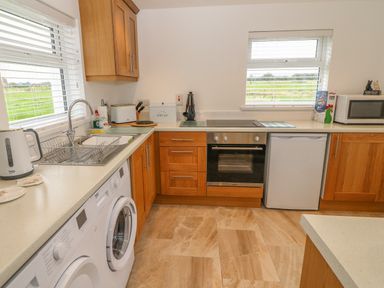 A kitchen with wooden cabinets a washing machine a toaster a microwave an oven and two windows showing green fields at Dirreen House Athea near Listowel County Kerry