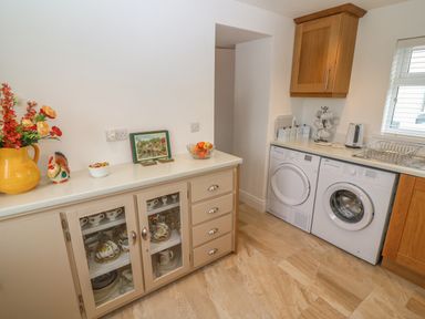 A laundry room with a washing machine and dryer a countertop with a kettle and dish rack and a cabinet with glass doors displaying dishes at Dirreen House Athea near Listowel County Kerry
