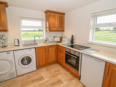 A kitchen with wooden cabinets a washing machine an oven and two windows showing a green field at Dirreen House Athea near Listowel County Kerry