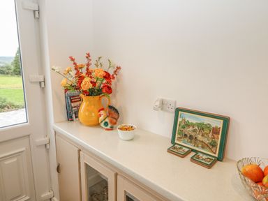A kitchen countertop with a yellow jug of flowers a ceramic rooster figurine a bowl of wrapped candies books and a set of coasters at Dirreen House Athea near Listowel County Kerry