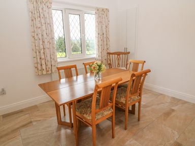 A dining room with a wooden table and six chairs near a window with floral curtains at Dirreen House Athea near Listowel County Kerry