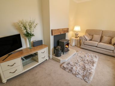 A living room with a beige sofa a wood stove and a TV on a cabinet at Dirreen House in Athea near Listowel County Kerry