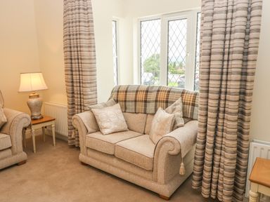 A sitting area with a beige couch a side table with a lamp and windows with curtains at Dirreen House Athea near Listowel County Kerry