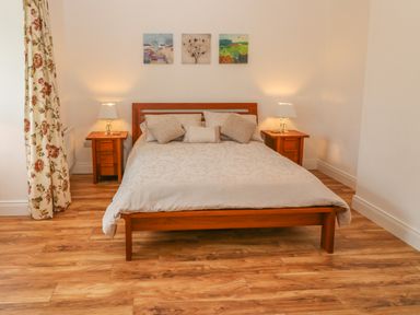 A bedroom with a wooden bed frame two bedside tables with lamps and three paintings above the bed at Dirreen House Athea near Listowel County Kerry