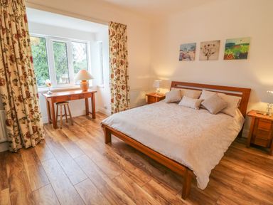 A bedroom with a wooden bed and bedside tables with lamps a wooden desk with a stool and floral curtains at Dirreen House in Athea near Listowel County Kerry