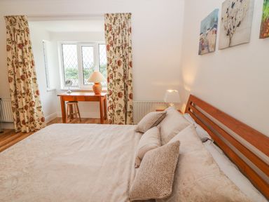 A bedroom with a bed cushions bedside table and lamp wooden desk stool and floral curtains at Dirreen House Athea near Listowel County Kerry