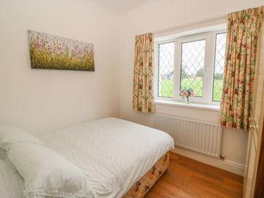 A bedroom with a bed a window with floral curtains and a flower vase on the sill at Dirreen House Athea near Listowel County Kerry