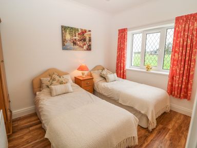 A bedroom with two single beds a wooden nightstand lamp and a window with red curtains at Dirreen House Athea near Listowel County Kerry
